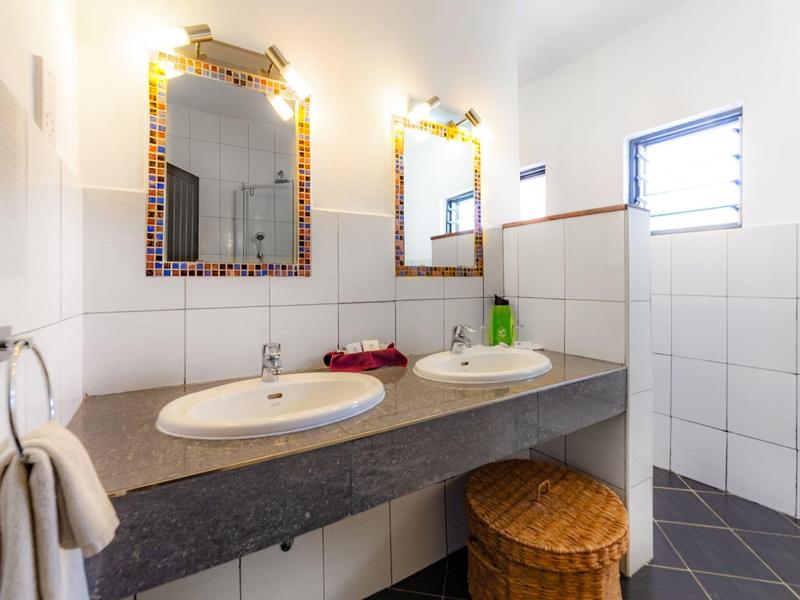 Licht badkamer met twee wastafels, decoratieve spiegels en wasmand onder het aanrecht.