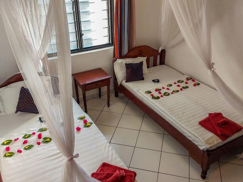 Twee eenpersoonsbedden met klamboes, versierd met bloembladeren en rode handdoeken.