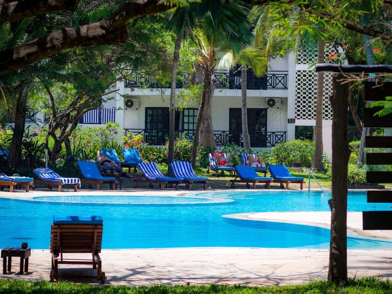 Blauw zwembad met ligstoelen in een rustige hoteltuin met bomen en planten.