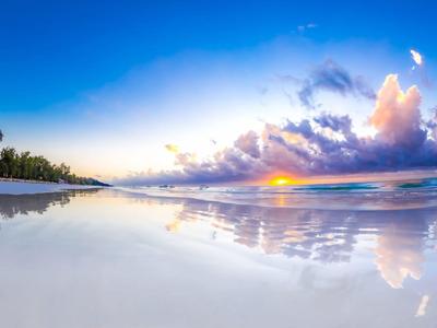 Sunset at calm beach with reflection in wet sand and cloudy sky.