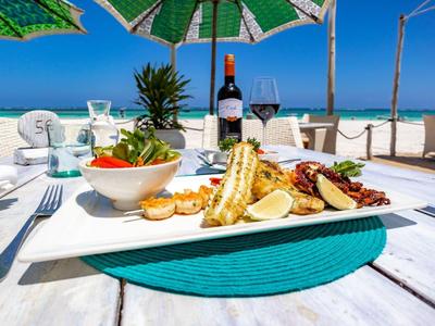 Table with sea view, served with fish dish, salad, and wine at a sunny beach.