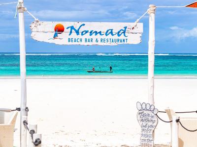 Beach with white sand and clear blue water, sign for Nomad Beach Bar & Restaurant.