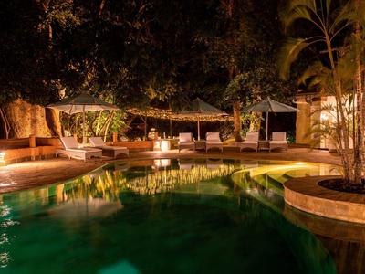 Illuminated hotel pool with seating areas and plants at night.