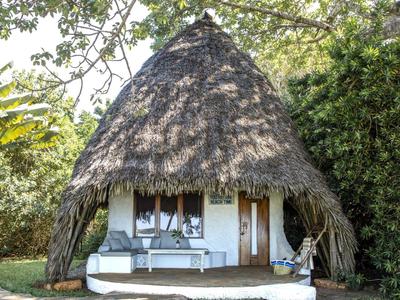 Small thatched hut with pointed roof and white veranda in a green setting.