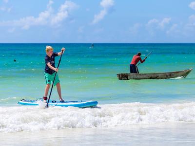 Person paddelt auf einem Stand-Up-Paddle-Board im Meer neben einem Mann in einem kleinen Boot.