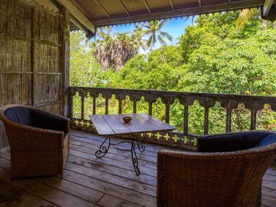 Cozy balcony with two wicker chairs and a table overlooking tropical trees.