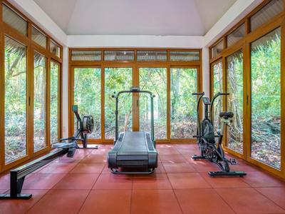 Fitnessraum mit Cardio-Geräten und Hantelbänken, umgeben von großen Fenstern mit Blick auf Grünfläche