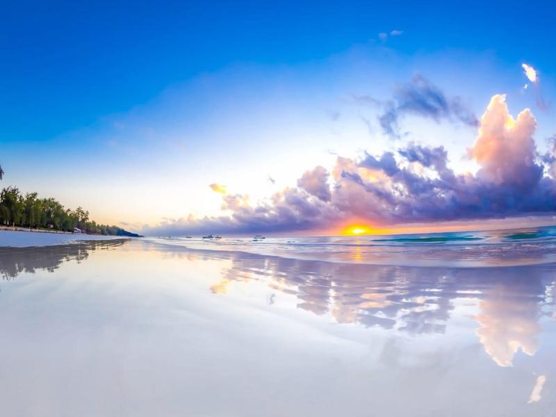 Sunset at calm beach with reflection in wet sand and cloudy sky.
