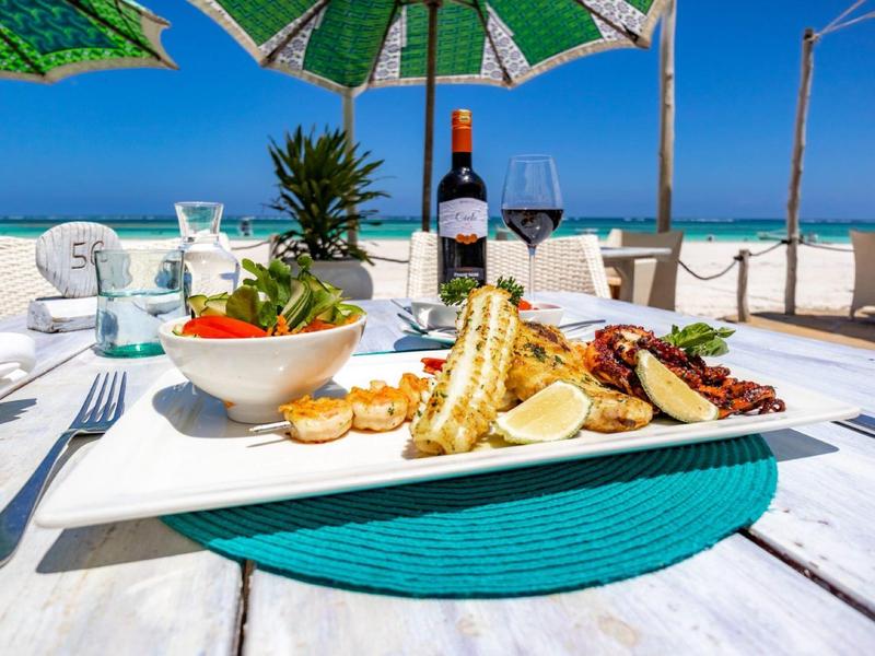 Table with sea view, served with fish dish, salad, and wine at a sunny beach.