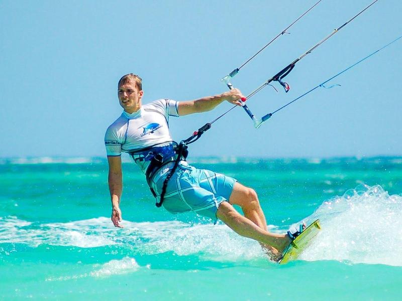 Man kiteboarding on turquoise sea under bright blue sky.