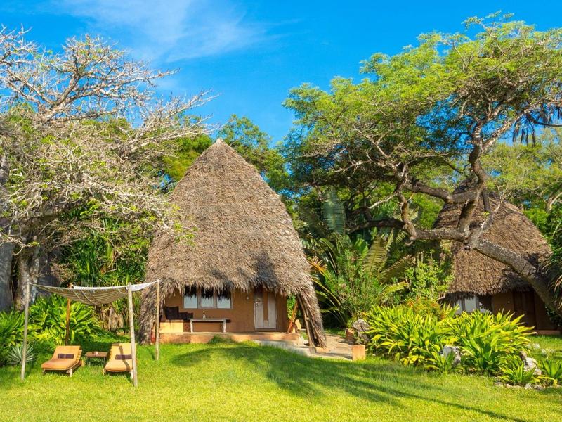 Traditional thatched huts in a tropical garden setting under a blue sky.