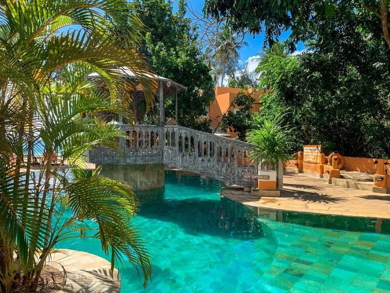 Clear water pool surrounded by greenery and seating areas, including a gazebo.