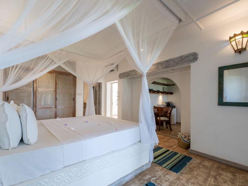 Bright bedroom with canopy bed, white curtains, and carpeted floor in a hotel room.