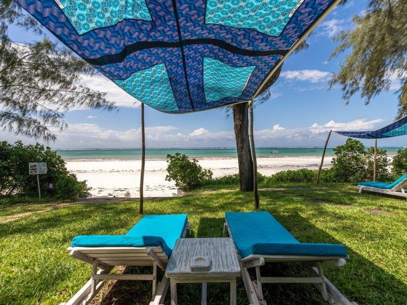 Two blue lounge chairs under a blue sunshade facing the beach and ocean.