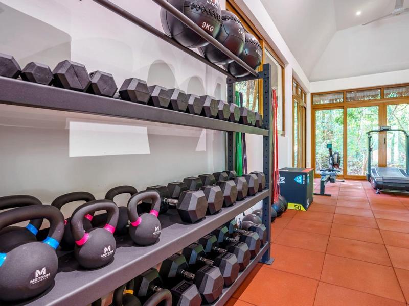 Bright gym with weights, kettlebells, and treadmill in front of large windows.