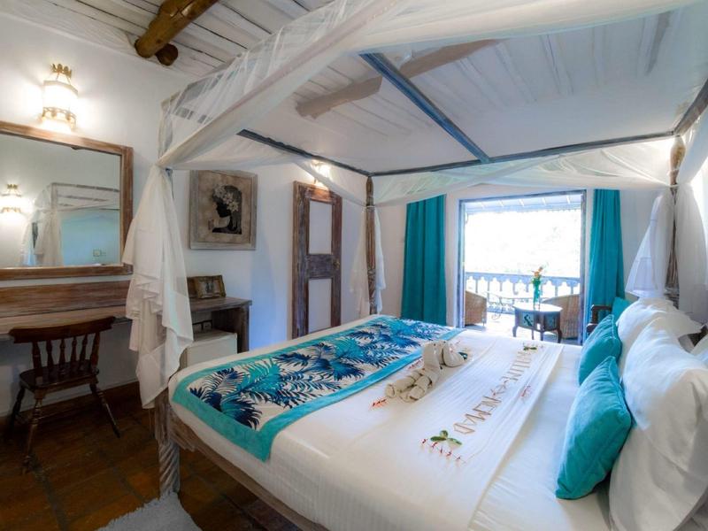 Cozy bedroom with wooden beams, double bed, mirror, and balcony with outdoor view.