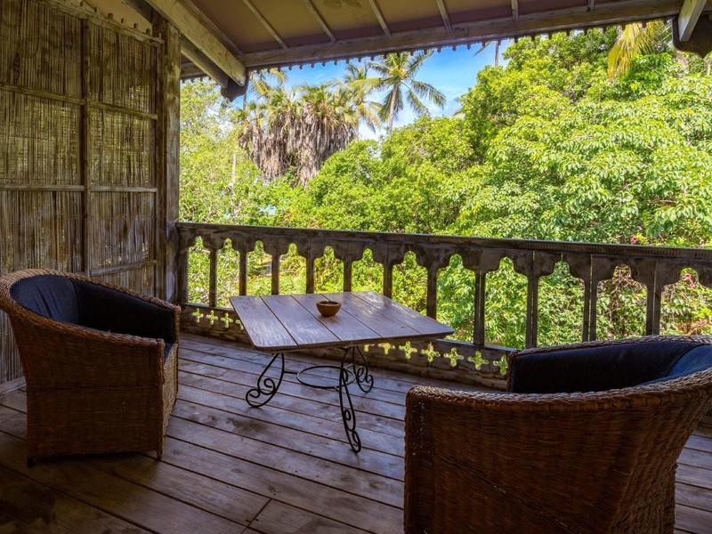 Cozy balcony with two wicker chairs and a table overlooking tropical trees.