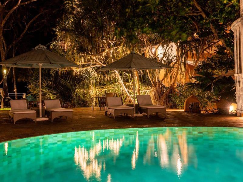 Illuminated pool area at night with umbrellas and outdoor furniture in a tropical setting.