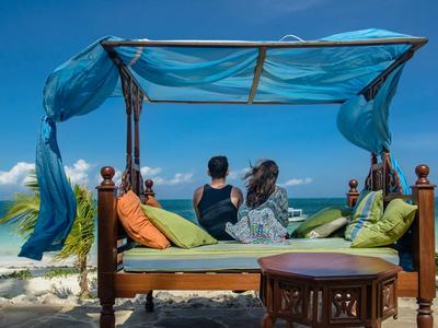Couple se détend sur un lit à baldaquin sur la plage avec vue sur l'océan et ciel bleu.