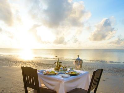 Deux chaises et une table dressée sur la plage au coucher du soleil.