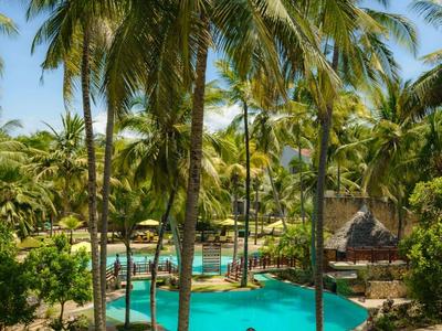 Chambre d'hôtel lumineuse avec lit double, coussins bleus et grande fenêtre donnant sur la terrasse.