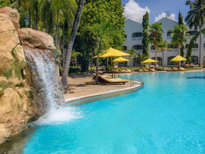 Piscine ensoleillée avec toboggan entourée de palmiers et de chaises longues dans une station tropicale.