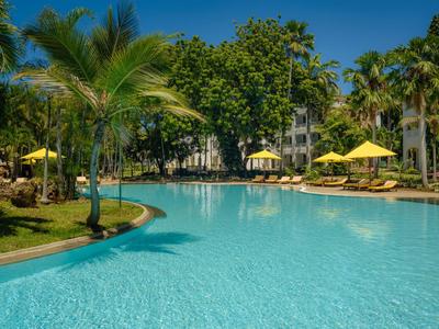 Grande piscine extérieure avec palmiers et parasols jaunes dans un jardin d'hôtel tropical.
