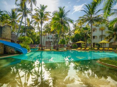 Piscina soleggiata con scivolo d'acqua circondata da palme e lettini in un resort tropicale.