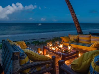 Coin salon confortable avec bougies et coussins sur la plage au coucher du soleil.