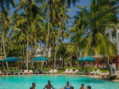 Six personnes se tiennent la main en formant un cercle dans une piscine entourée de palmiers.