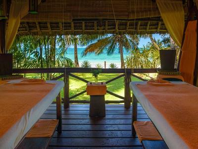 Deux tables de massage confortables sous un toit de chaume avec vue sur les palmiers et le ciel bleu.