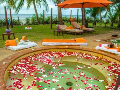 Personne se détendant dans un bain de pétales près de la piscine avec palmiers et vue sur la mer.