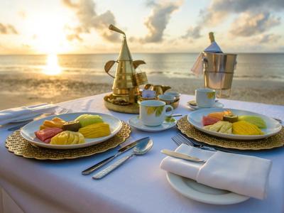 Petit-déjeuner romantique avec assiette de fruits et thé sur la plage au lever du soleil.