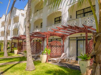 Vue extérieure d'un hôtel blanc avec balcons et palmiers par temps ensoleillé.