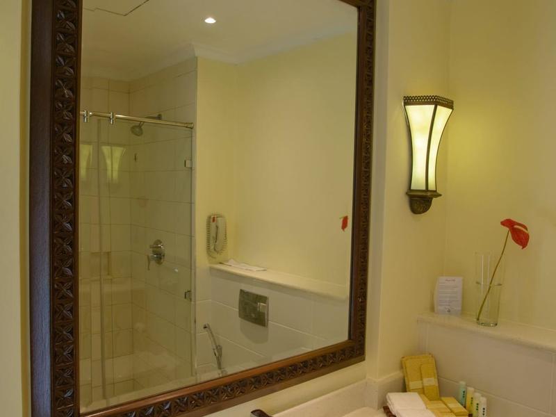 Grand miroir de salle de bain avec lavabo, savon, lotion et lampe murale.