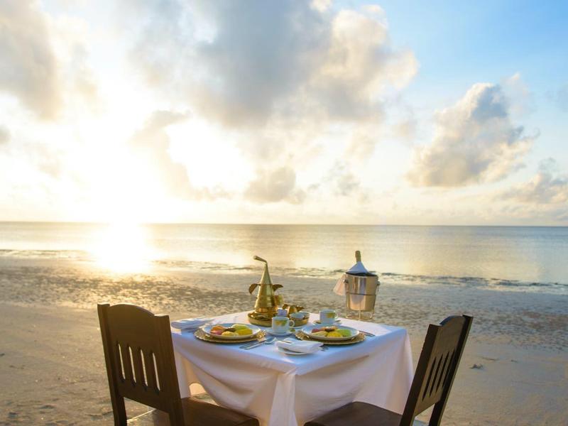 Deux chaises et une table dressée sur la plage au coucher du soleil.