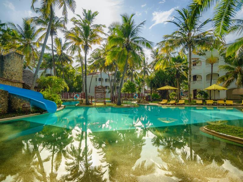 Piscine ensoleillée avec toboggan entourée de palmiers et de chaises longues dans une station tropicale.