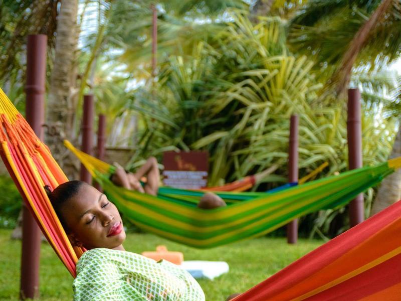 Personne se détendant dans un hamac coloré sous des palmiers en ambiance tropicale.