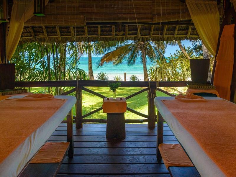 Deux tables de massage confortables sous un toit de chaume avec vue sur les palmiers et le ciel bleu.
