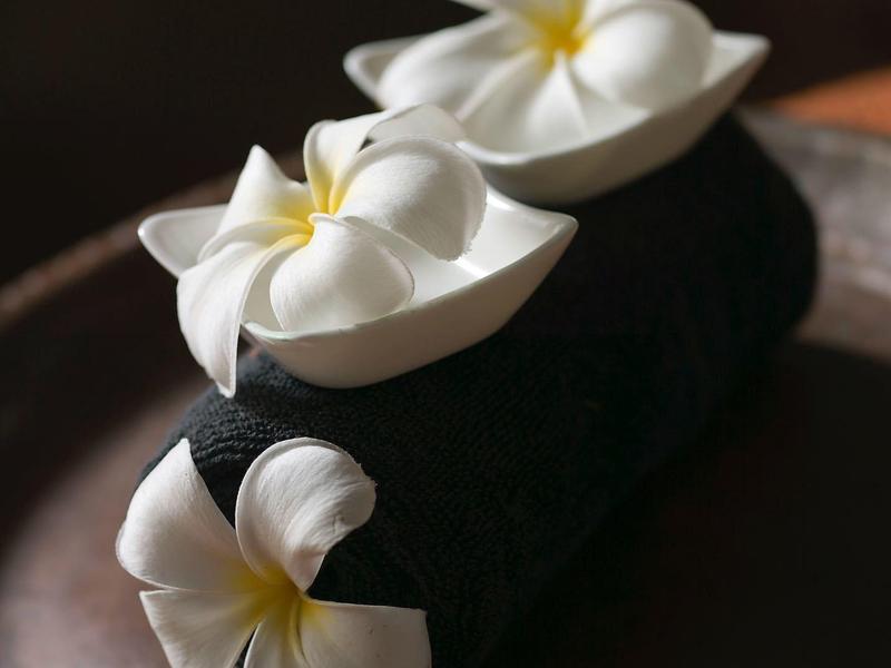 Tre fiori bianchi appoggiati su un asciugamano nero posato su un vassoio marrone.
