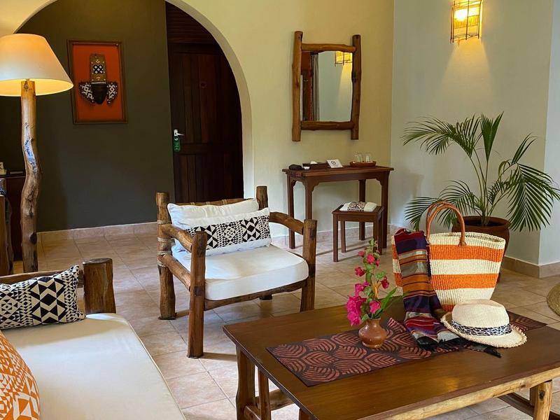 Zona giorno con poltrone bianche, tavolo in legno, divano con cuscini e decorazioni dai colori caldi.