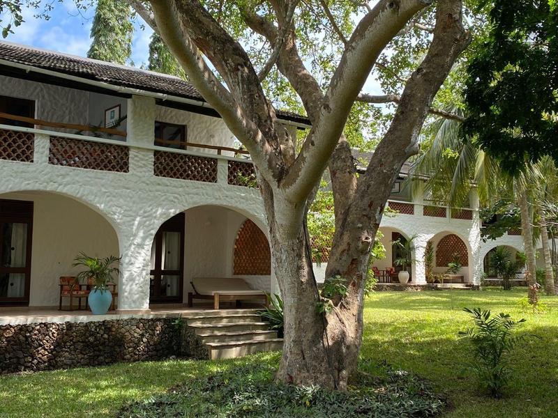 Edificio bianco con archi e veranda, circondato da alberi e prato.