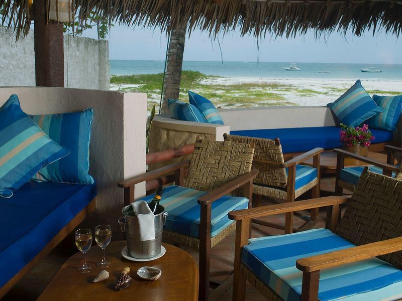 Lounge coperta con mobili in legno e cuscini a righe blu con vista sulla spiaggia.