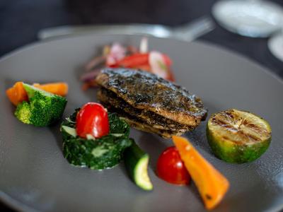 Ein Teller mit gegrilltem Fisch, Gemüse und einer Zitronenscheibe, dekorativ angerichtet.