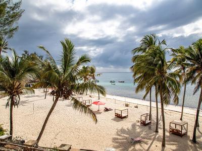 Strand mit Palmen, Sand und Liegen am Meer unter einem bewölkten Himmel.