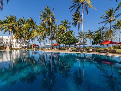 Ein großer Pool umgeben von Palmen und roten Sonnenschirmen unter klarem blauem Himmel.