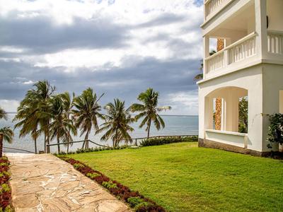 Pfad führt an einem weißen Hotel mit Blick auf Palmen und Meer vorbei unter bewölktem Himmel.