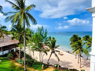 Blick von einem Balkon auf einen tropischen Strand mit Palmen, Sand und Meer unter blauem Himmel.