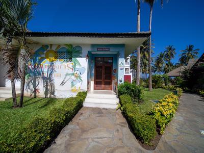 Eingang eines Hotels mit bunt bemalter Wand, Palmen und gepflegtem Gartenweg unter blauem Himmel.