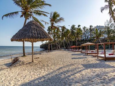 Weißer Sandstrand mit Palmen, Strohdachhütte und Liegen am tropischen Hotelstrand.